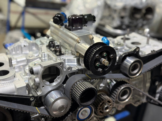 Dry sump oil pump mounted on a Subaru EJ engine block with toothed drive pulley, timing belt and AN fittings
